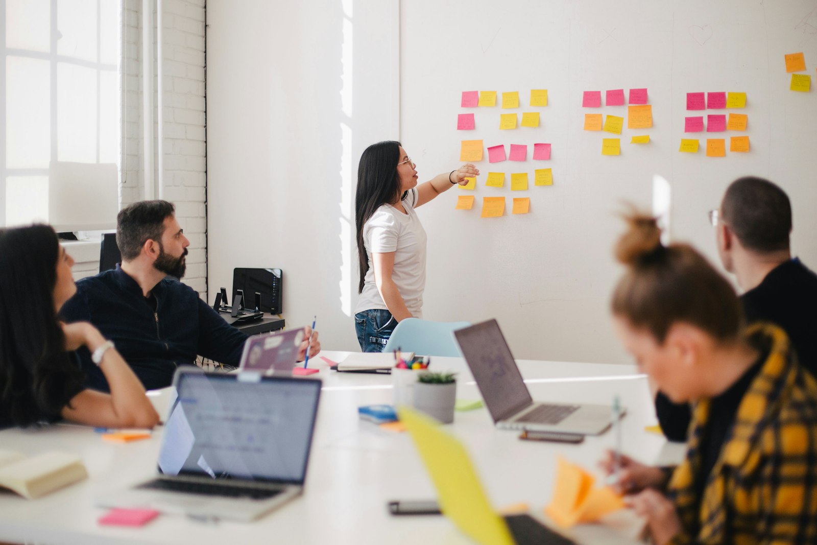 Engineer mapping a workflow on a wall of sticky notes while teammates work at laptops